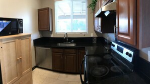 A kitchen with wooden cabinets, a black countertop, a stainless steel sink, a microwave, and a stove. - Luxury Casita at Desert Estate in Scottsdale (Scottsdale)