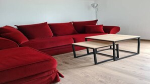 Un canapé d’angle rouge, accompagné d’une table basse en bois, se trouve dans une pièce aux murs blancs et au plafond en pente.