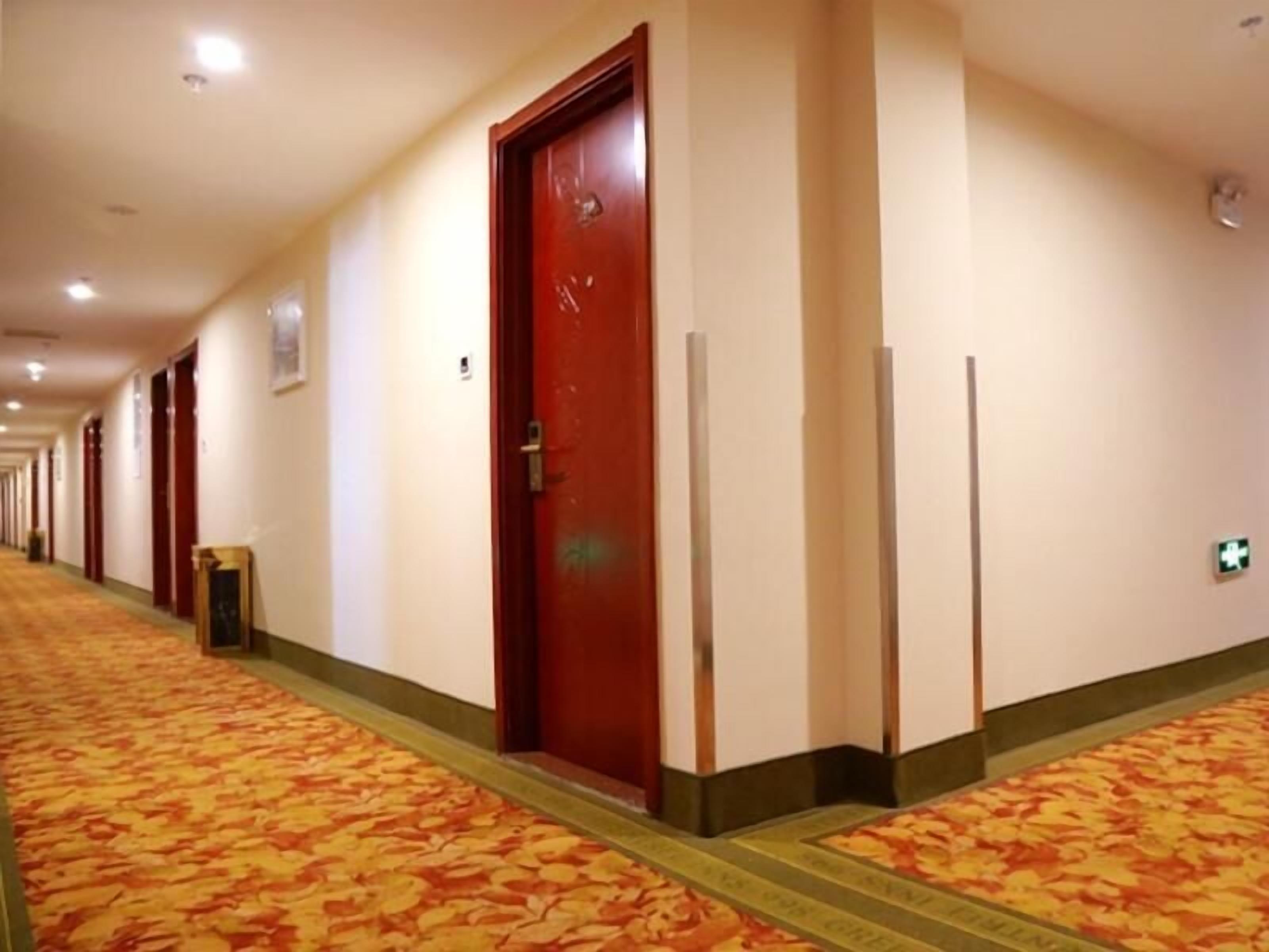 A hotel corridor with a patterned carpet, red doors, and a green emergency exit sign.