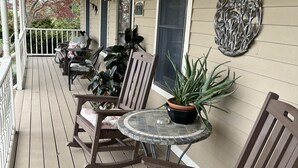 A covered porch with wooden furniture, including chairs and a table, and a potted plant.