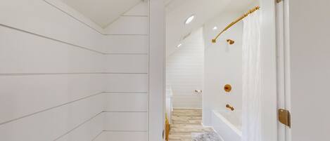 Un pasillo con paneles blancos, suelo de madera y una bañera blanca con detalles dorados.