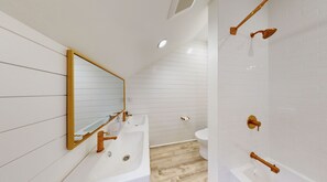 Ein modernes Badezimmer mit einem großen Spiegel, zwei Waschbecken, einer Toilette und einer Dusche mit goldenen Armaturen.