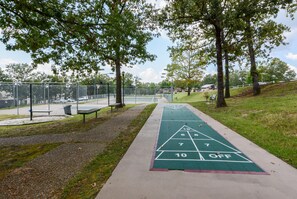 A shuffleboard court with a green surface and white markings, surrounded by trees and a fence. - Suite Outlook Penthouse near Downtown (Branson)