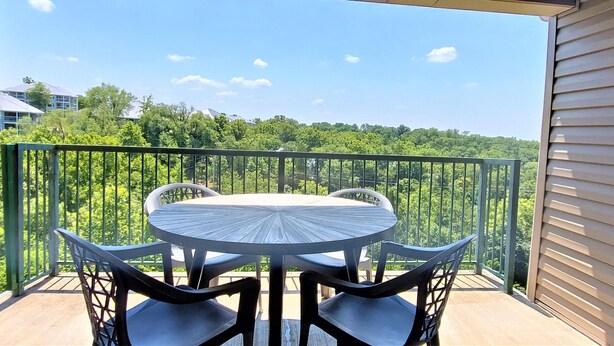 Ein Balkon mit rundem Tisch und vier Stühlen, mit Blick auf ein bewaldetes Gebiet.