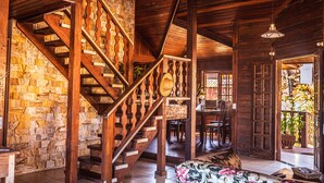 Una escalera de madera con un muro de piedra de fondo, un área de comedor con muebles de madera y vistas al exterior.
