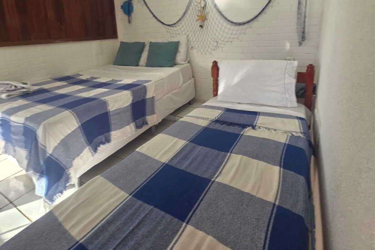 Ein Zimmer mit zwei Betten, einem Holz-Kopfteil, einer weißen Wand mit einer Zierleiste und einem Fenster mit einer Holzjalousie.