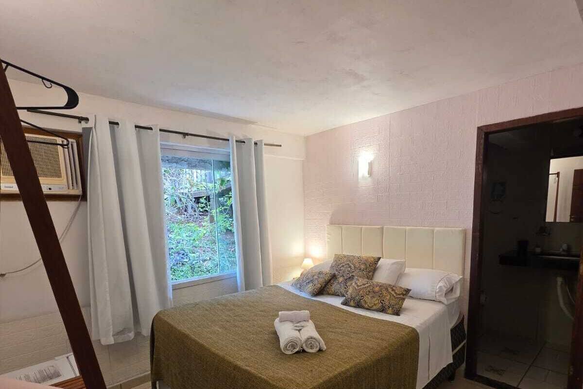 Ein Schlafzimmer mit Bett, Vorhängen am Fenster, einem Nachttisch und einer Lampe.