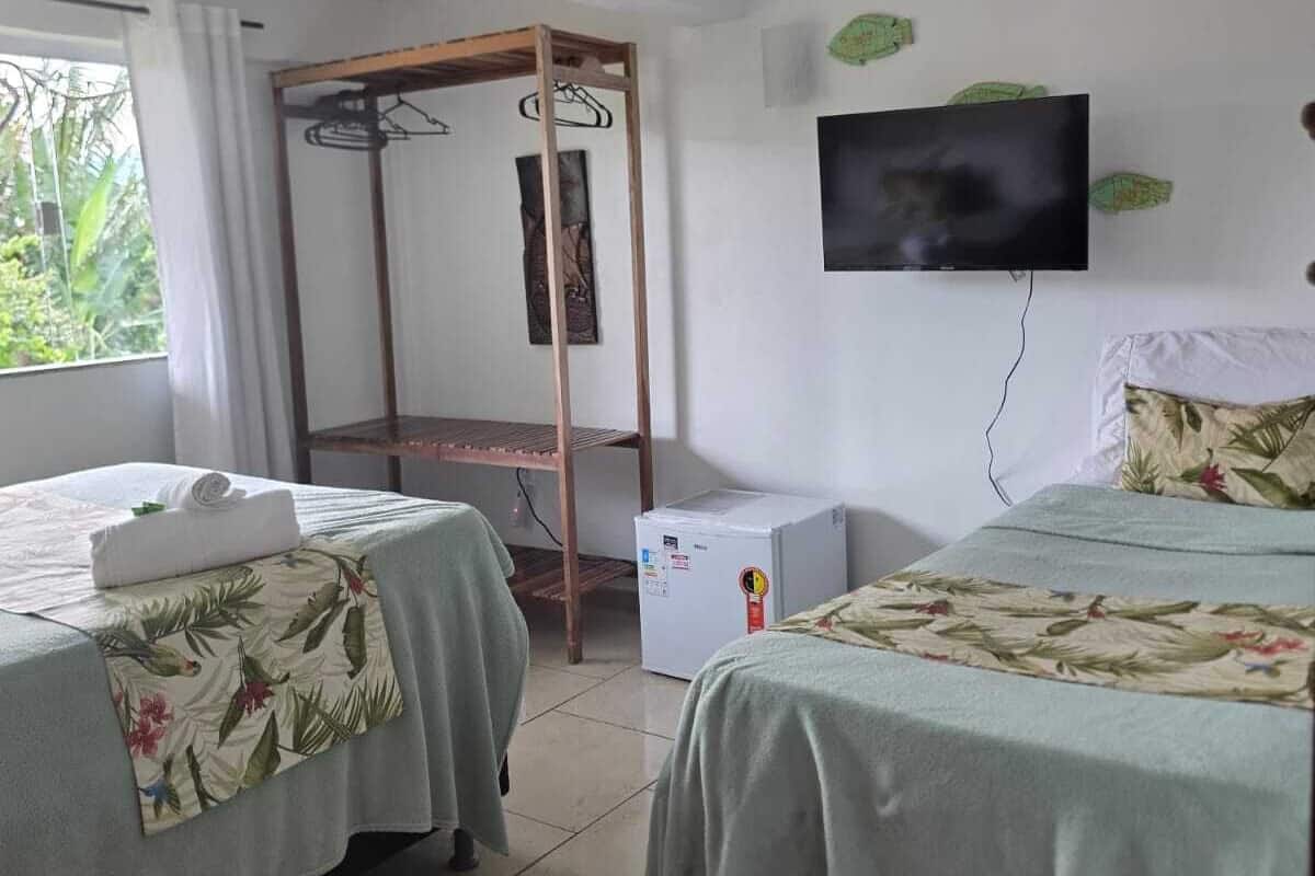 Ein Hotelzimmer mit zwei Betten, einem Fernseher, einer kleinen Kühlbox und einem Fenster mit Vorhängen.