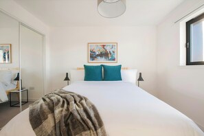 Relax in a serene space with a large bed, a stylish ceiling light, and a beautiful abstract art piece.