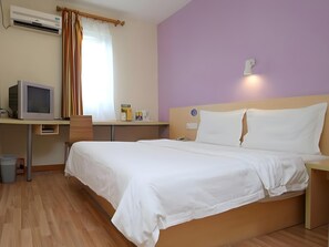 Habitació d'hotel amb un llit, una taula de treball amb un ordinador, una finestra amb cortines i un aparell d'aire condicionat.