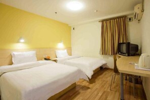 Habitació d'hotel amb dos llits, una taula petita amb una papereta, televisió i finestra amb cortines.