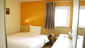 A single-bed room with a white bed, a bedside table with a lamp, a window with a striped curtain, and a small picture on the wall. - 7 Days Inn Shenzhen Longhua Branch (Shenzhen)