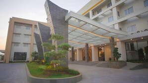 A modern building with a curved facade, a covered entrance, and a landscaped courtyard with trees. - Pollos Hotel & Gallery Rembang (Rembang)