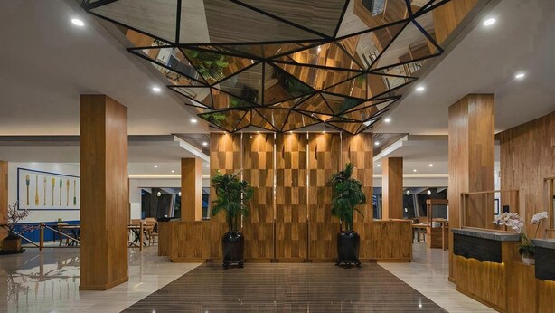 A modern lobby with a geometric ceiling design, wooden reception desk, and potted plants. - Pollos Hotel & Gallery Rembang (Rembang)