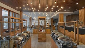 A buffet setup with multiple serving stations, wooden paneling, and pendant lighting. - Pollos Hotel & Gallery Rembang (Rembang)