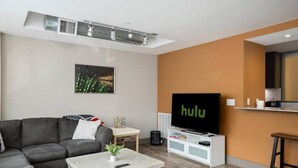 Una sala de estar moderna con un sofá seccional gris, una mesa de centro, un televisor de pantalla plana y una pequeña mesita auxiliar blanca.