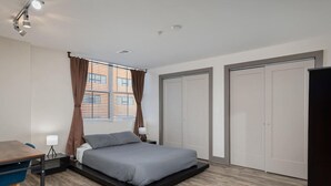 Un dormitorio moderno con una cama, un escritorio y una silla. Hay dos armarios y una ventana con cortinas.