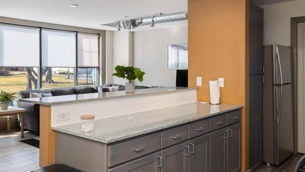 Una cocina moderna con una isla grande, armarios oscuros y un refrigerador de acero inoxidable.