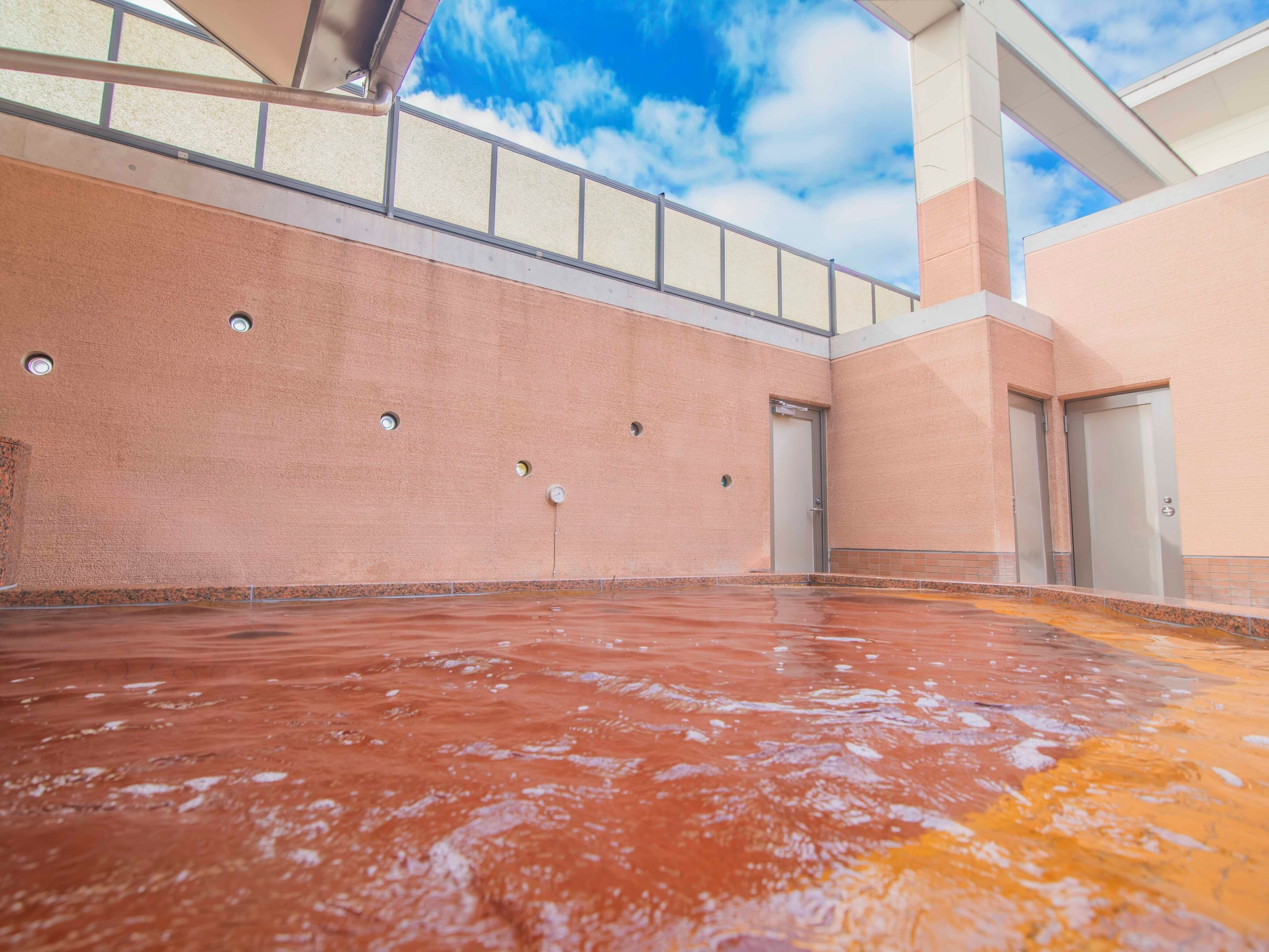 Un área de piscina interior amplia con vistas despejadas al cielo gracias a un techo de cristal, suelo de baldosas y techo alto con barandilla metálica.