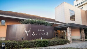 A building with a curved sign featuring Japanese characters and a deer logo, surrounded by greenery and a paved entrance area. - FLEXSTAY INN Kashima Central (Kamisu)