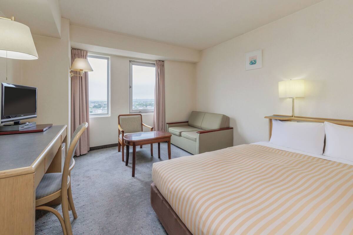 Une chambre d’hôtel comprenant un lit, un bureau, une chaise, un canapé et un téléviseur.