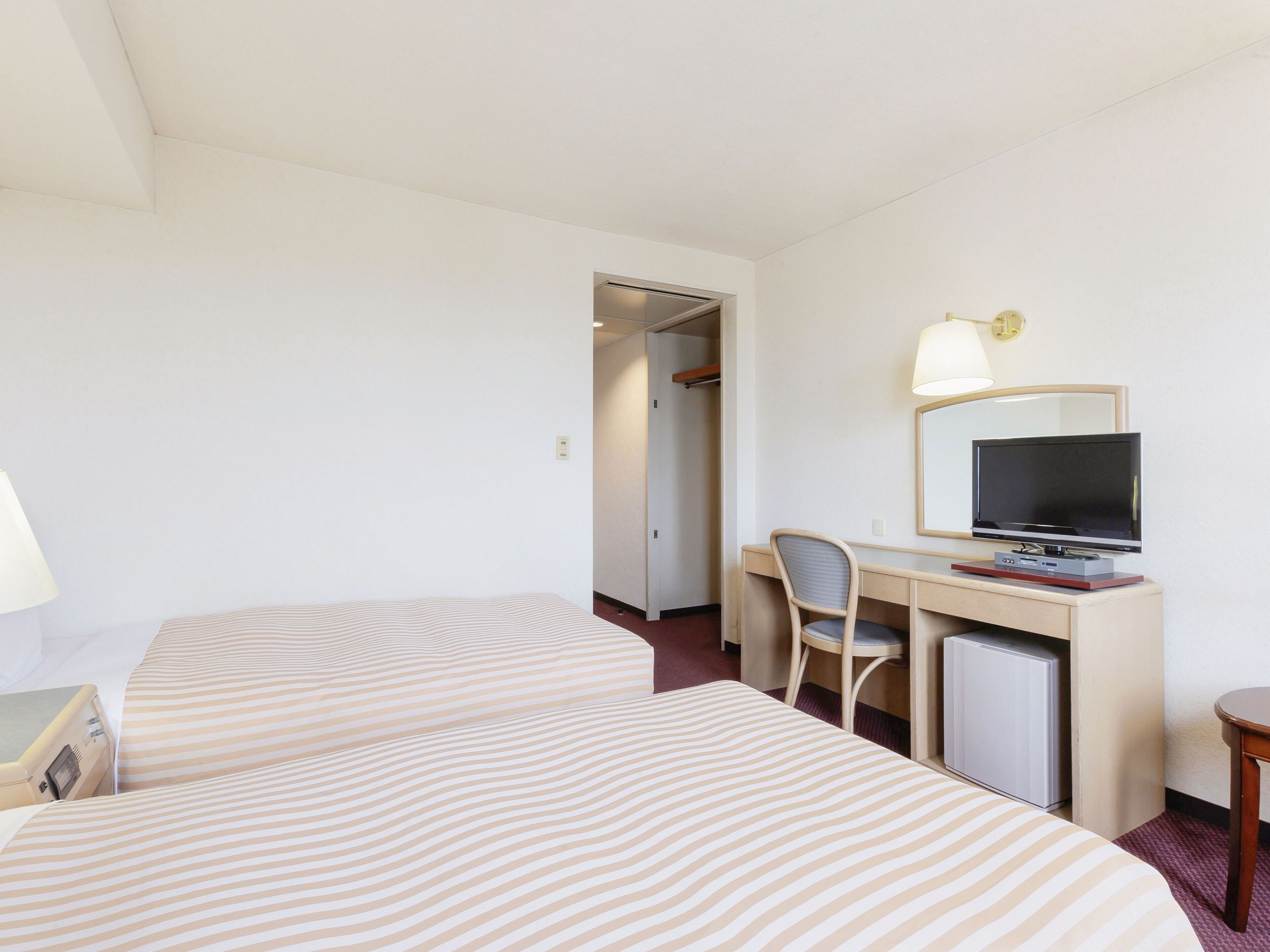 Une chambre d’hôtel avec deux lits, un bureau avec un ordinateur, une télévision et une lampe.