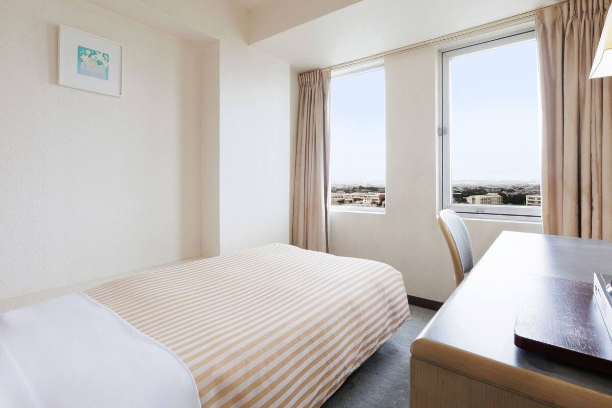Une chambre d’hôtel avec un lit, un bureau et une fenêtre donnant sur la ville.