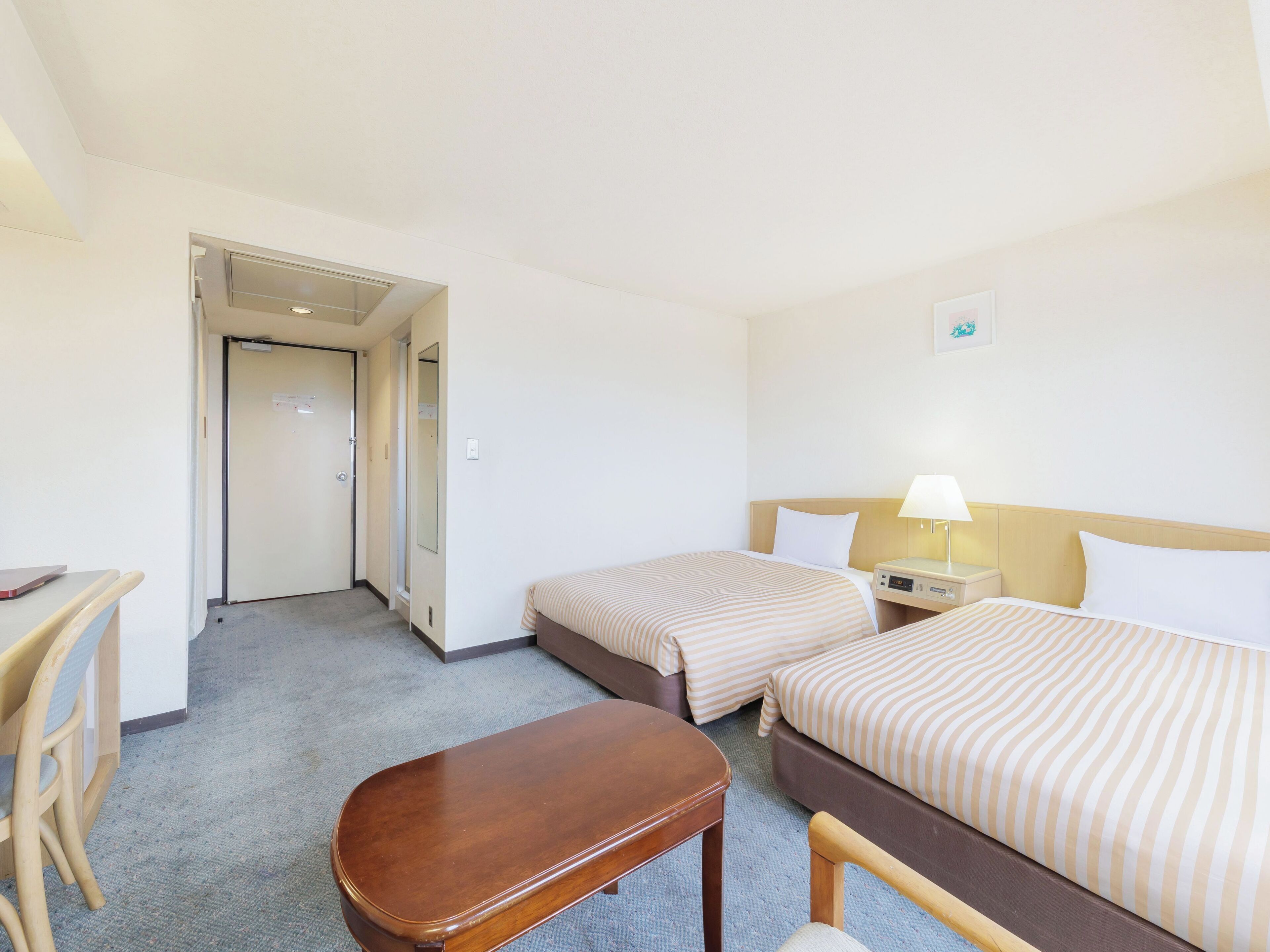 A hotel room with two beds, a desk, a chair, and a lamp.