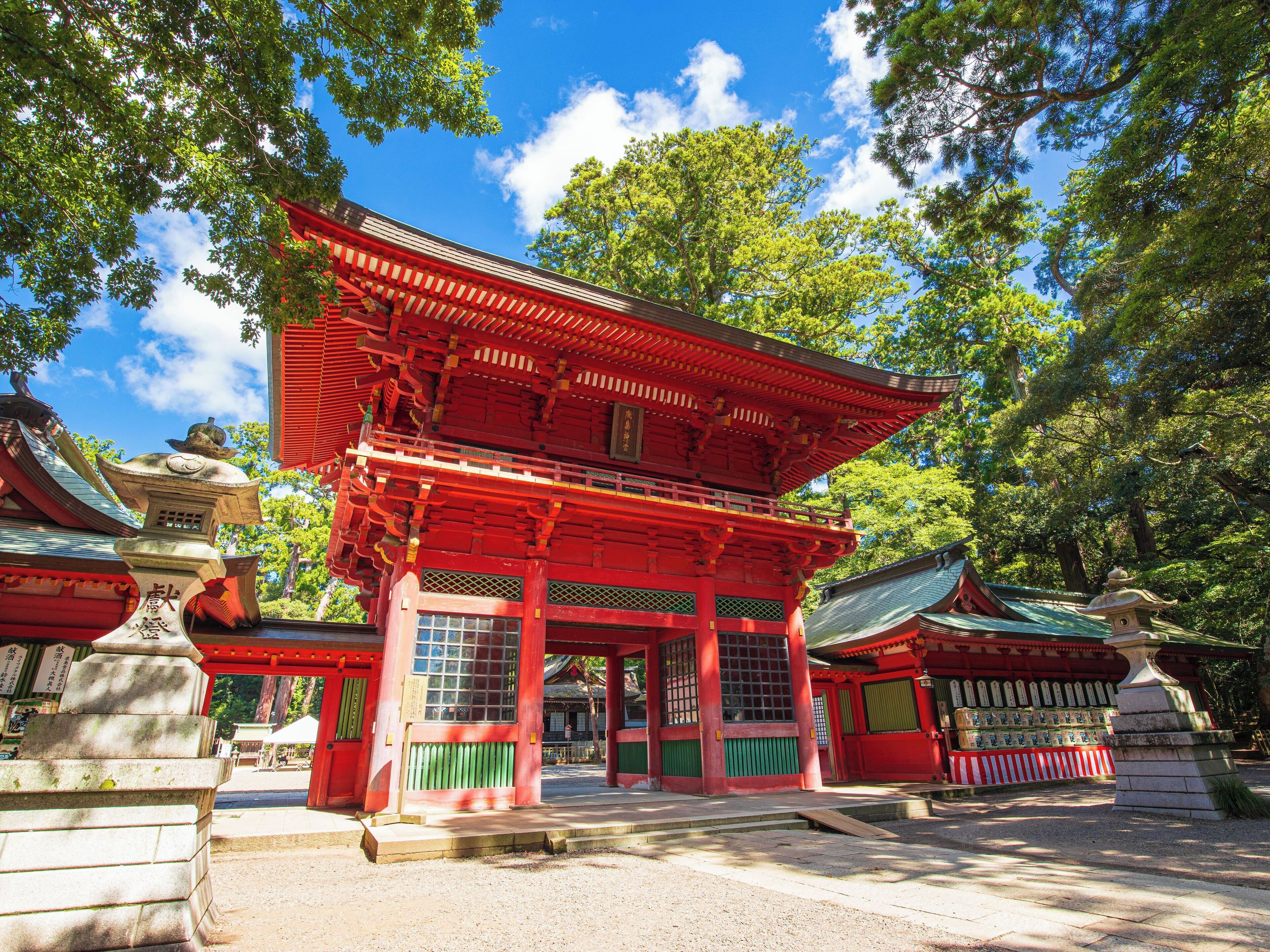 A traditional Japanese temple with a red main building, surrounded by trees and a clear sky.