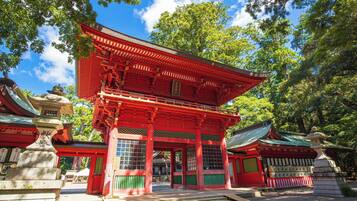 A traditional Japanese temple with a red main building, surrounded by trees and a clear sky.