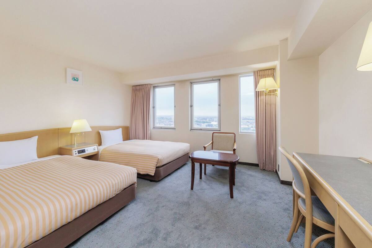 Une chambre d’hôtel avec deux lits, un bureau et une chaise.