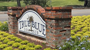 A brick sign with "True Blue Golf Club" written on it, surrounded by well-maintained landscaping.