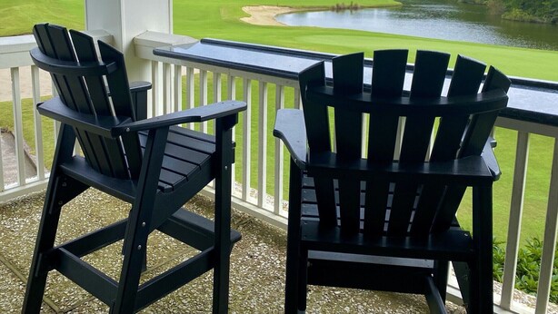 Two Adirondack chairs on a balcony overlooking a golf course and a lake.