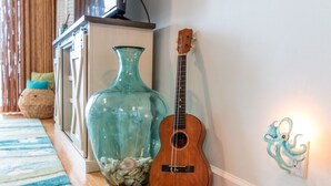 Une piÚce avec un plancher en bois, un grand vase turquoise rempli de pierres, une guitare en bois et un luminaire fixé au mur.