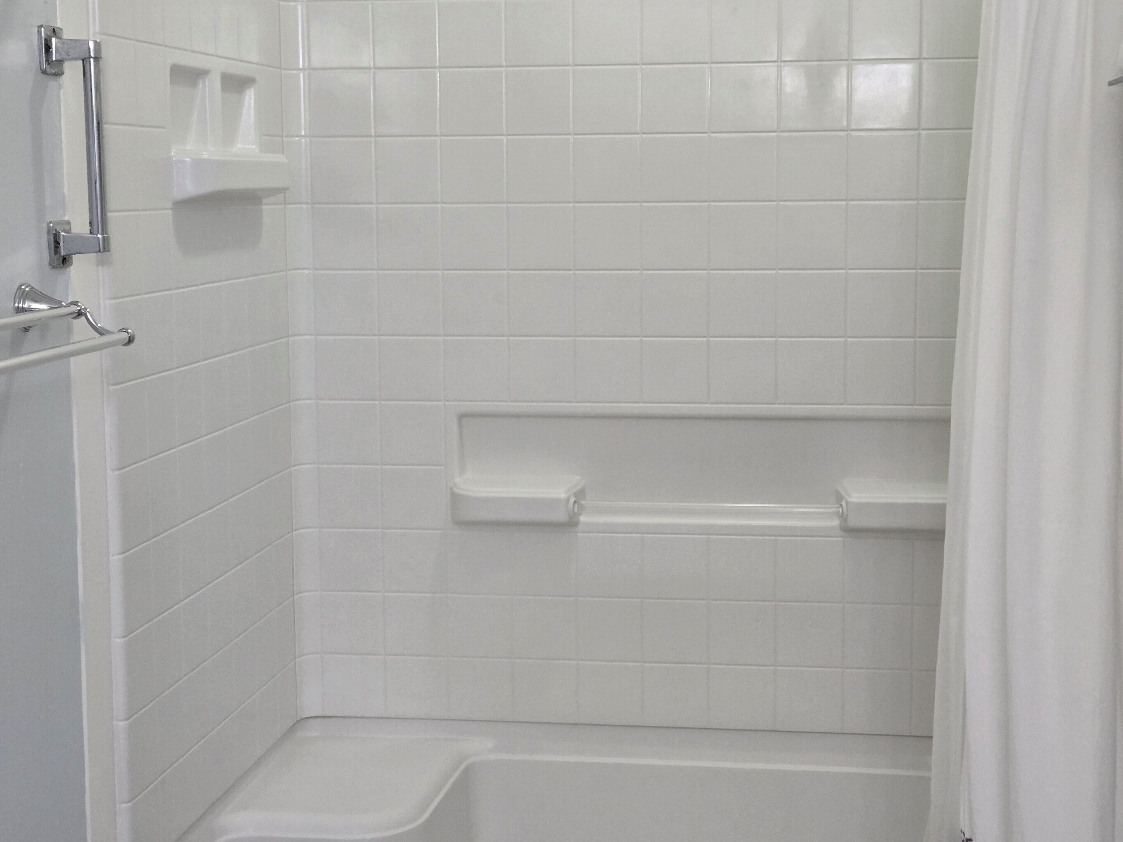 Un baño con paredes de azulejos blancos, una bañera y una cortina de ducha.
