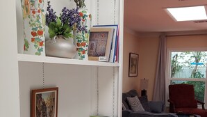 Un saló amb una biblioteca blanca, un sofà gris i un butac armchair vermell. Hi ha elements decoratius a les prestatgeries, com ara florejadors i marcs de fotos.