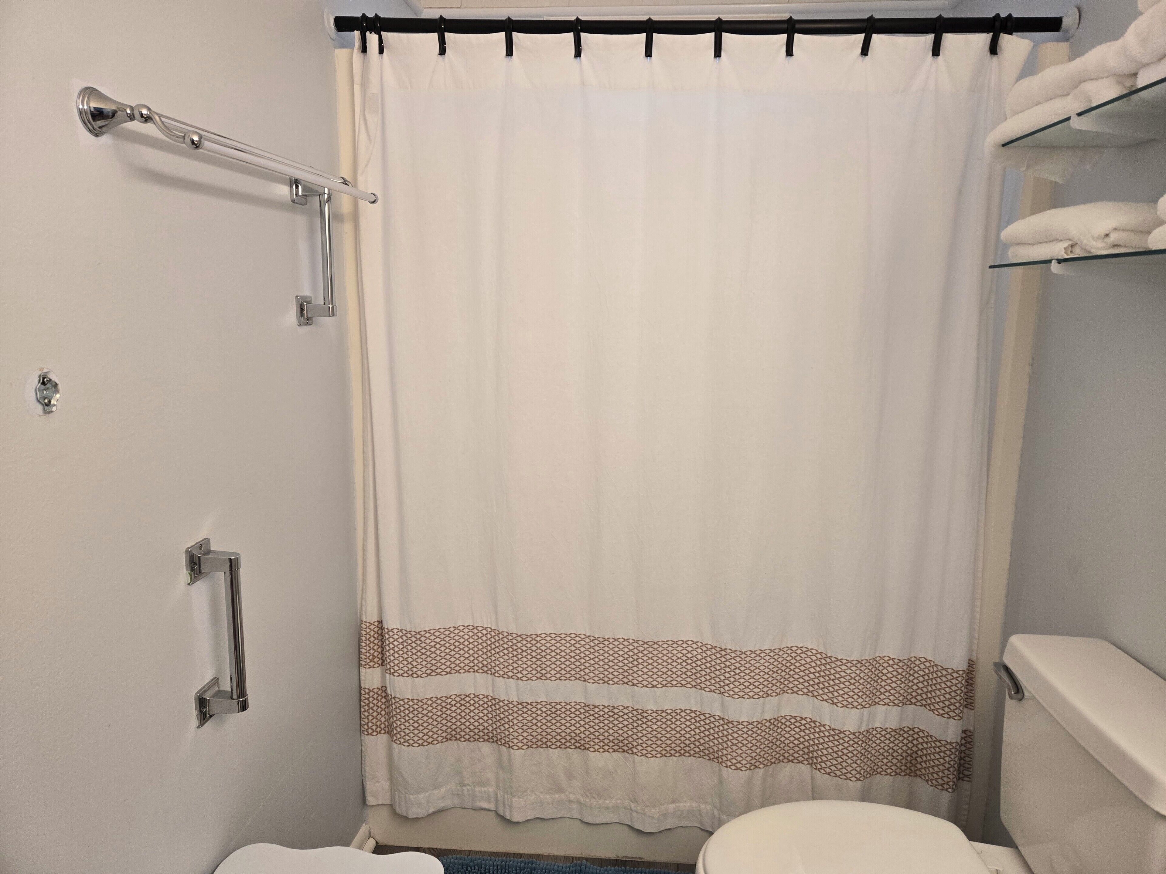 A bathroom with a white shower curtain, a white toilet, and a towel rack with towels.