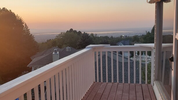 Une terrasse en bois avec une balustrade blanche, d’où l’on peut admirer le paysage urbain au coucher du soleil.