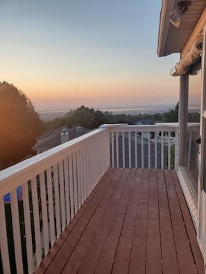 Una terraza de madera con barandilla blanca que da a una vista panorámica de la ciudad al atardecer.