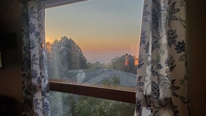 Une fenêtre ornée de rideaux à motifs floraux, une vue sur un quartier résidentiel et un coucher de soleil.