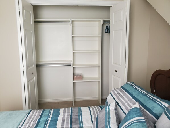 Un dormitorio con cama, almohada a rayas, armario con las puertas abiertas y cabecero de madera.