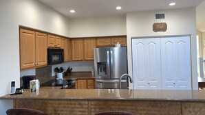 A kitchen with wooden cabinets, a stainless steel refrigerator, a microwave, and a double door closet. - Stunning ocean view Ali'i Cove J-1 (Kailua Kona)