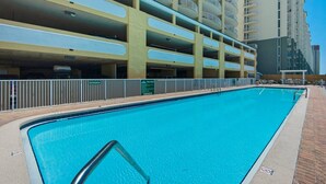 A swimming pool with a metal railing, a multi-story parking garage, and a high-rise building in the background. - Twin Palms 1103 (Panama City Beach)