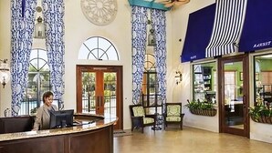 A hotel lobby with a reception desk, patterned curtains, and a view of the street outside.