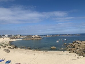 A coastal beach with clear waters, rocky outcrops, and a few boats.