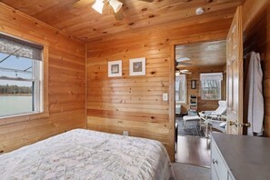 A wooden cabin bedroom with a bed, a small desk, and a chair. - Sand Lake Peninsula Getaway - Sandy Beach (Webster)