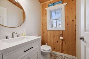 A bathroom with a wooden wall, a white sink with two faucets, a toilet, and a window above the toilet. - Sand Lake Peninsula Getaway - Sandy Beach (Webster)