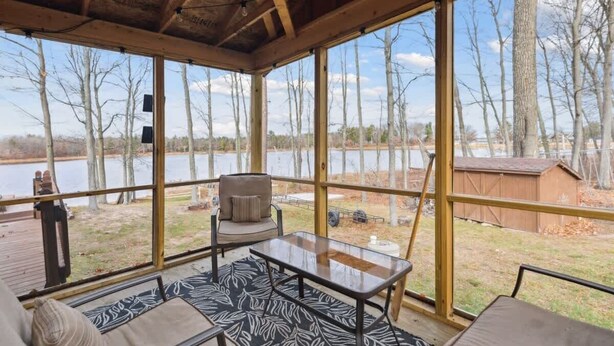 Un espacio de estar techado al aire libre con vistas a un lago y árboles.