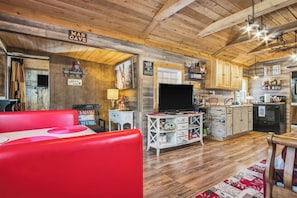 A cozy interior with a red sofa, wooden ceiling, a TV, and a kitchen area. - RRR Cabin on the Medina | 1800 Feet River | Deer (Medina)