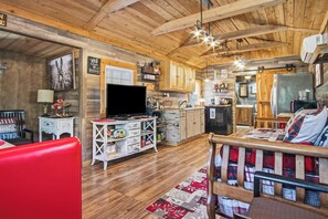 A cozy interior with wooden beams, a television, kitchen area, and a red sofa. - RRR Cabin on the Medina | 1800 Feet River | Deer (Medina)